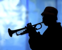 a person playing the trumpet, silhouetted against a blue background