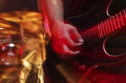 a hand playing an electric guitar, bathed in red light