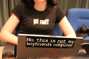A woman works on her laptop. It bears a sticker saying: no, this is not my boyfriend's computer.