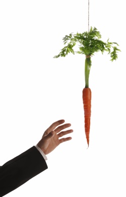 the arm of a person in a suit reaches for a dangling carrot